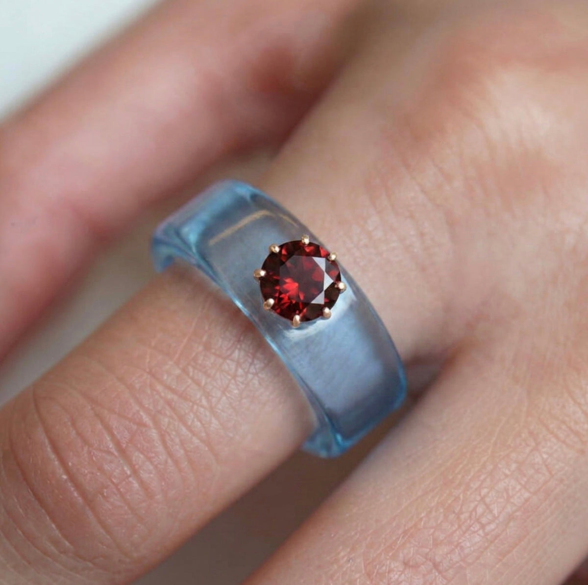 Anillo CG de granate y resina celeste, puesto en la mano